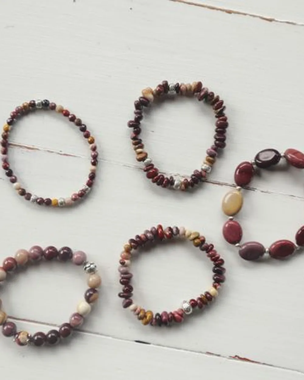 Cinq bracelets de perles posés sur du bois blanc