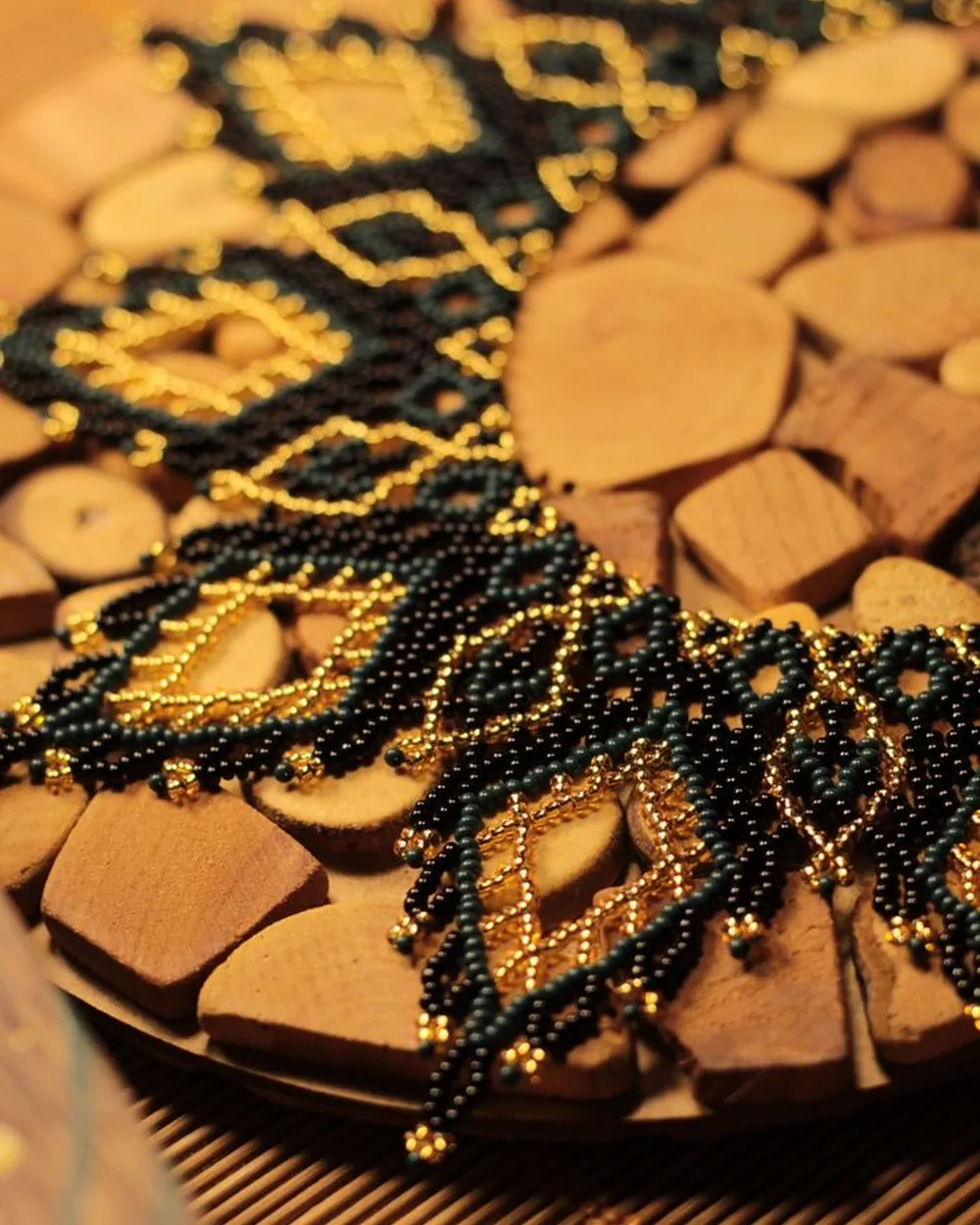 Collier tissé de perles noires et dorées, posé sur un plateau en bois