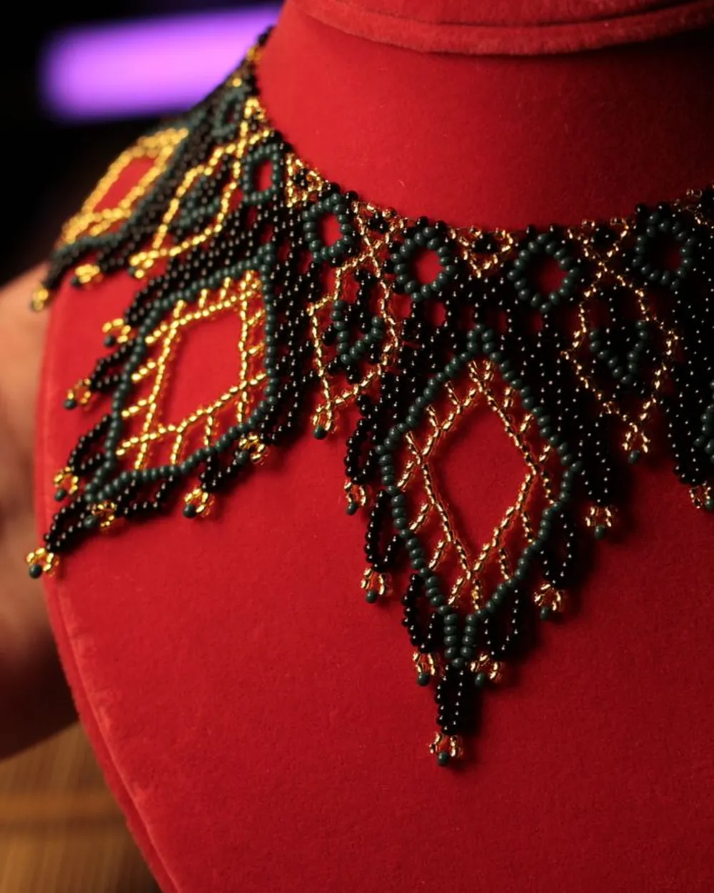 Plastron de perles noires et dorées à motifs de losanges, sur un buste