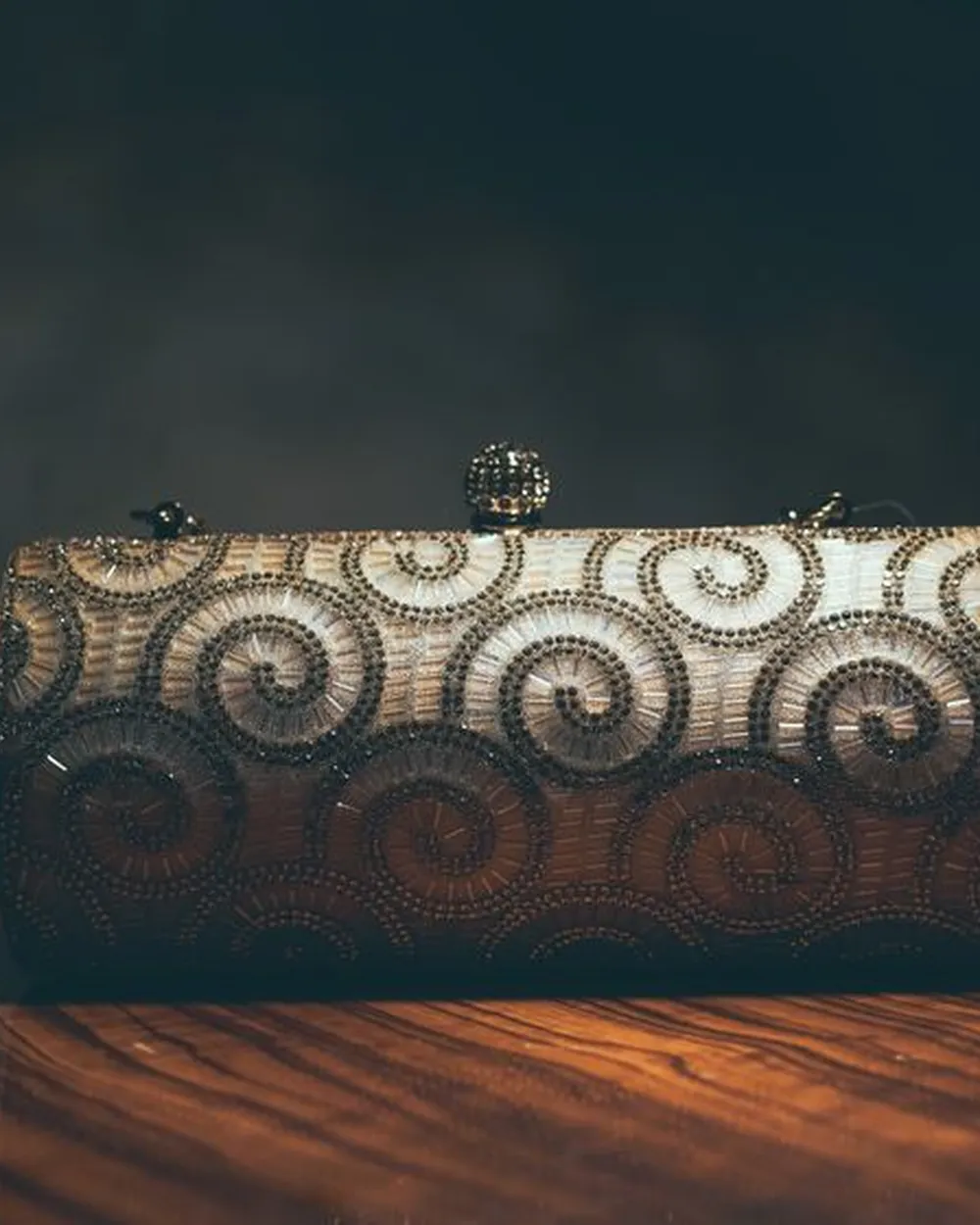 Minaudière rigide brodée de spirales, posée sur une table en bois